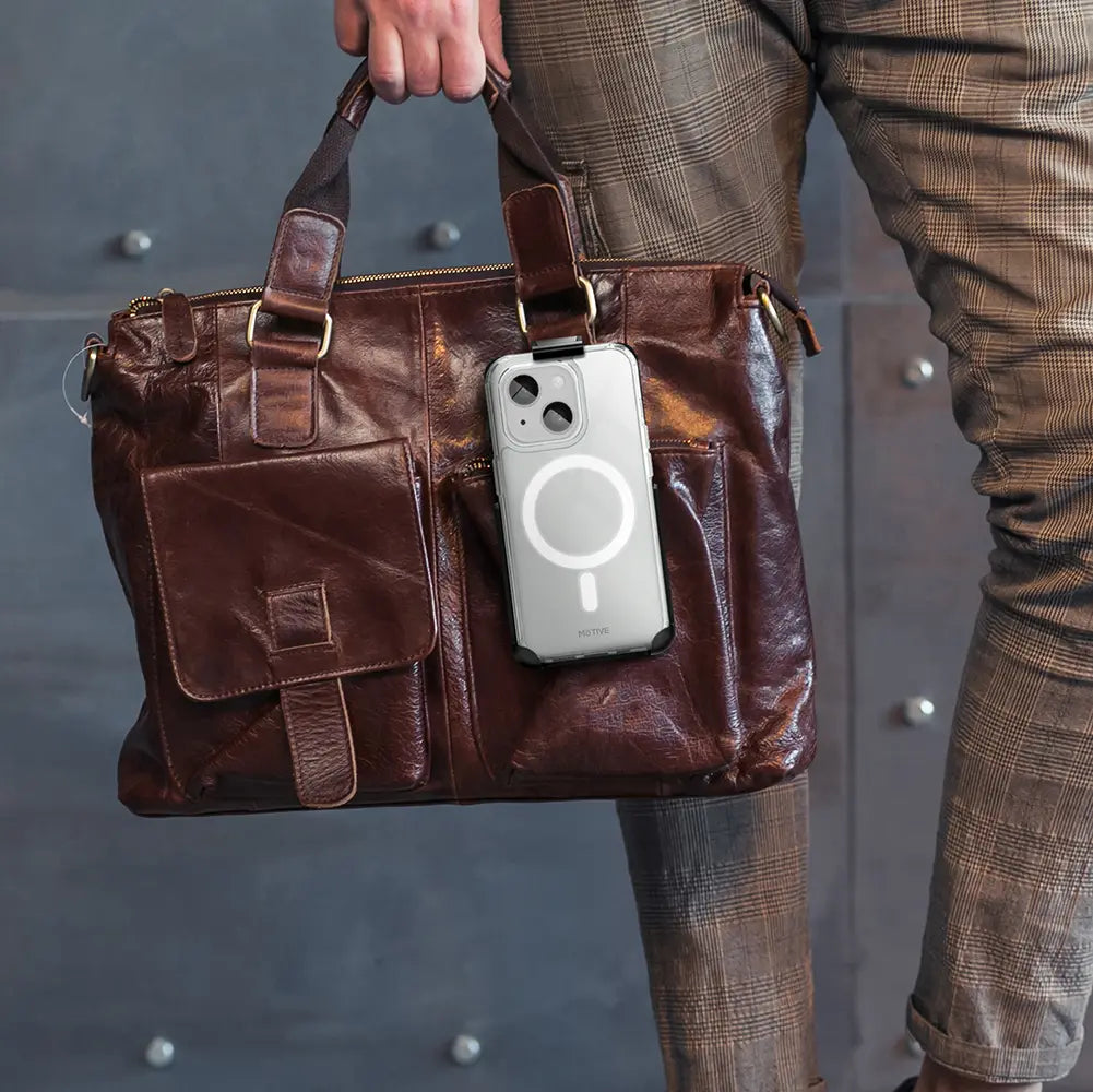 Clear iPhone 15 Plus case with belt clip attached to brown leather bag.