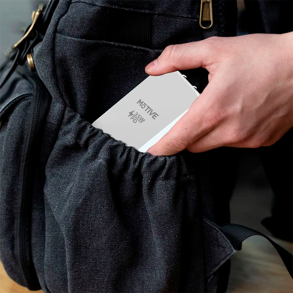 Flat dual port USB-C and USB-A wall charger being placed into a bag pocket.