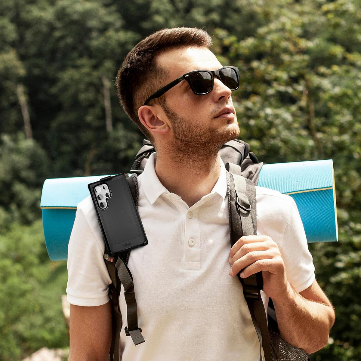 Male hiker exploring outdoors wearing Motivecase Bunker heavy-duty case for Samsung Galaxy S23 Ultra attached securely to backpack strap clip holster.